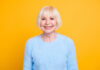 Featured image showing a healthy and happy woman in her 70's smiling against a yellow backdrop.